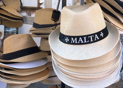 Masse hatter i beige farge med hattebånd det står Malta på. - Klikk for stort bilde